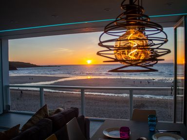 A dining and living area with a view of the beach and ocean at sunset at Louies Loft in St Ives