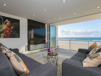 A living room with two sofas a small table a wall-mounted TV and a view of the beach at Louies Loft in St Ives