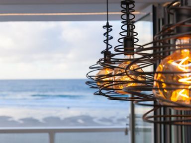A close up of hanging light bulbs with a view of the sea through a window at Louies Loft in St Ives