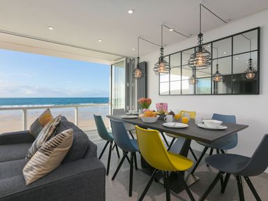 A dining area with a black table set with food and drinks next to a gray sofa facing a beach view at Louies Loft in St Ives