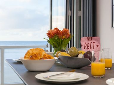 A dining table with croissants in a bowl orange flowers juice glasses and decorative fruits at Louies Loft in St Ives