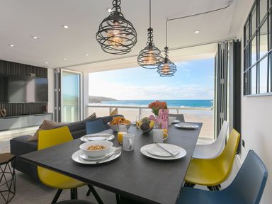 A dining table with plates cups and fruit bowls in a room with large windows overlooking a beach at Louies Loft in St Ives
