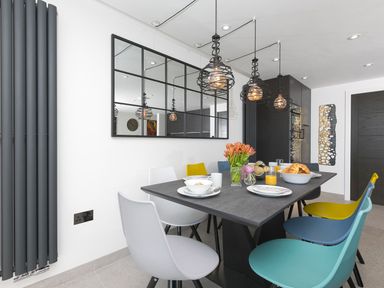 A dining area with a dark table and multicolored chairs with breakfast items and flowers at Louies Loft in St Ives