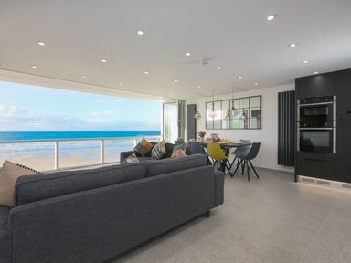 An open plan living room and kitchen with sofas, dining table, chairs, and a view of the beach at Louies Loft in St Ives
