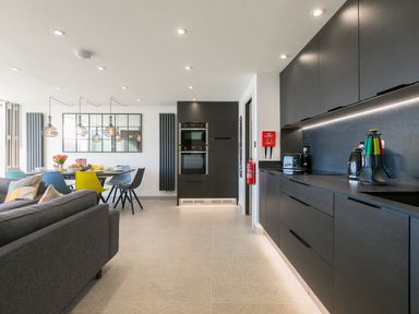 A modern kitchen and dining area with dark cabinets and a table with colorful chairs at Louies Loft in St Ives