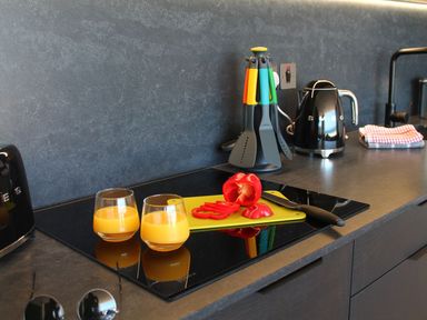 A kitchen countertop with two glasses of orange juice a sliced red bell pepper on a cutting board a knife cooking utensils a black kettle and folded cloths at Louies Loft in St Ives