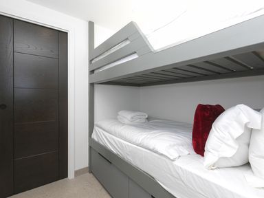 A bedroom with a grey bunk bed a black sliding door and folded towels on the bottom bed at Louies Loft St Ives