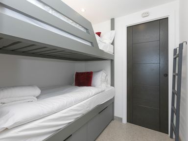 A small bedroom with grey bunk beds white bedding red pillows a black sliding door and a ladder at Louies Loft in St Ives