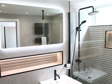 A bathroom with a lit mirror sink black faucet glass shower enclosure and black shower fixtures at Louies Loft in St Ives