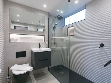 A bathroom with a wall-mounted sink, a toilet, a walk-in shower with glass partition, and a large mirror at Louies Loft in St Ives