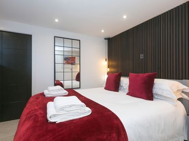 A bedroom with a bed with red pillows and a red throw blanket with towels on top at Louies Loft in St Ives