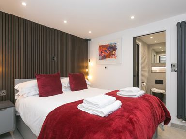 A bedroom with a double bed red pillows and blanket towels on the bed a nightstand and an open door to a bathroom at Louies Loft in St Ives