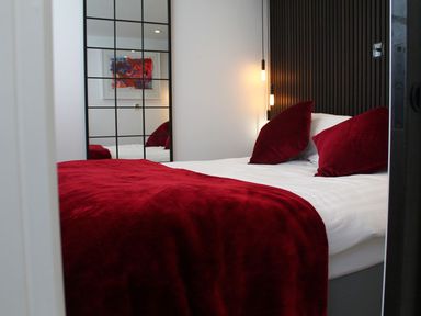 A bedroom with a bed covered in red pillows and a red blanket next to a mirror with grid lines at Louies Loft in St Ives