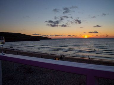 A beach view at sunset with people on the sand and in the water and a glass on a railing at Louies Loft in St Ives