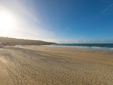 A sandy beach with footprints waves and a coastal town under a clear blue sky at Louies Loft in St Ives