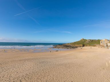 A sandy beach with footprints sea waves rocks and a small hill with buildings at Louies Loft in St Ives