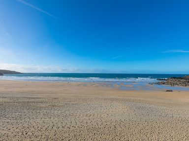 A sandy beach with footprints and ocean waves under a blue sky at Louies Loft in St Ives
