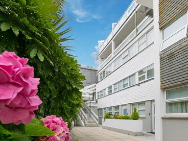 An apartment building with white siding windows and stairs next to a garden with pink flowers at Louies Loft in St Ives