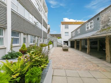 An outdoor courtyard with plants on the left and a covered parking area on the right at Louies Loft in St Ives
