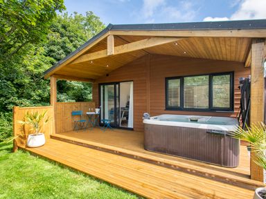 An outdoor wooden deck with a hot tub blue table and chairs and sliding glass doors at Maple Lodge in Angarrack