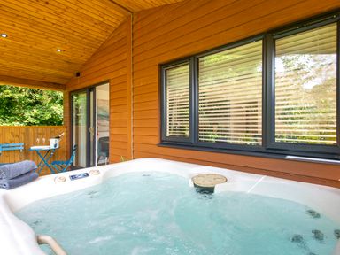 An outdoor covered deck with a hot tub towels a blue table and chairs and sliding glass door at Maple Lodge in Angarrack
