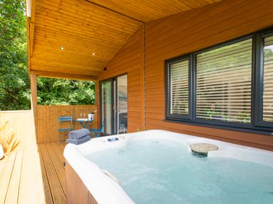 An outdoor covered wooden deck with a hot tub and a small blue table and two chairs at Maple Lodge in Angarrack