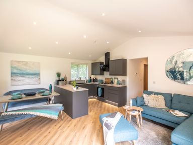 An open plan kitchen and living room with gray cabinets wooden floor teal sofa and dining table at Maple Lodge in Angarrack