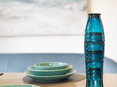 A blue glass bottle next to stacked turquoise plates on a table at Maple Lodge in Angarrack