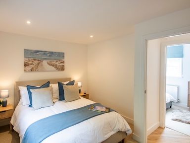 A bedroom with a bed and pillows and a painting on the wall next to a doorway showing another bedroom at Maple Lodge in Angarrack