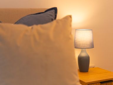 A blue table lamp on a wooden bedside table behind pillows on a bed at Maple Lodge in Angarrack