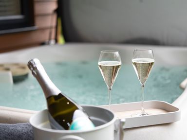 A bottle of champagne in an ice bucket and two filled champagne flutes by a hot tub at Maple Lodge in Angarrack