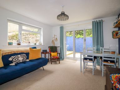 A sitting room with a blue sofa yellow cushions wooden chair and a dining table with chairs at 1 Mill Cottages in Porthtowan