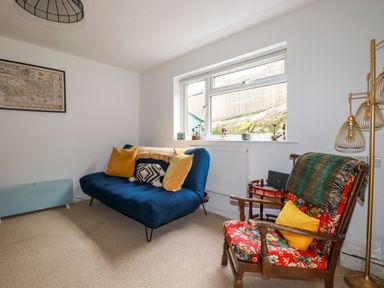 A living room with a blue sofa and yellow pillows and a floral armchair with a green blanket and yellow cushion at 1 Mill Cottages in Porthtowan