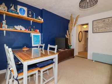 A dining area with a wooden table and chairs against a blue wall with shelves and decorations at 1 Mill Cottages in Porthtowan