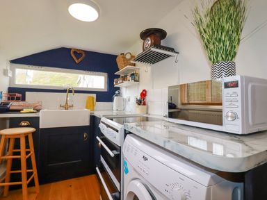 A small kitchen with a sink stove microwave washing machine and various utensils at 1 Mill Cottages Porthtowan