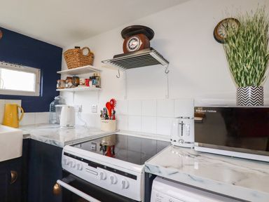 A kitchen corner with a stove kettle toaster microwave shelves with jars and a basket at 1 Mill Cottages in Porthtowan