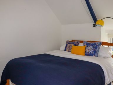 A bedroom with a bed with blue and yellow pillows and a blue blanket at 1 Mill Cottages in Porthtowan