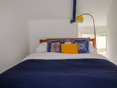 A bedroom with a bed with blue and yellow pillows and a yellow floor lamp at 1 Mill Cottages in Porthtowan