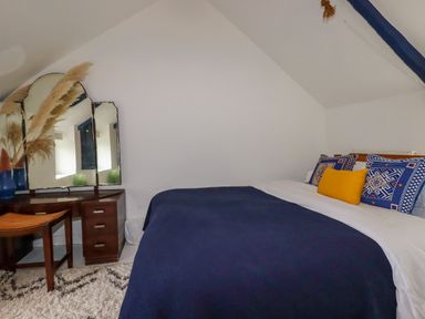 A bedroom with a bed with blue and white bedding a wooden dressing table with a three-panel mirror and a chair at 1 Mill Cottages Porthtowan