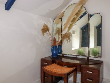 A wooden dressing table with a three-panel mirror a blue vase with dried plants and a woven seat stool at 1 Mill Cottages in Porthtowan