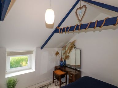 A bedroom corner with a dressing table chair mirror and window under a slanted ceiling at 1 Mill Cottages Porthtowan