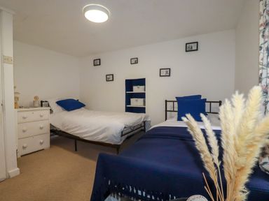 A bedroom with two single beds with blue and white bedding a small dresser and framed pictures on the wall at 1 Mill Cottages in Porthtowan