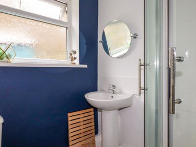 A bathroom with a pedestal sink a round mirror a shower enclosure and a window with decorative items at 1 Mill Cottages in Porthtowan