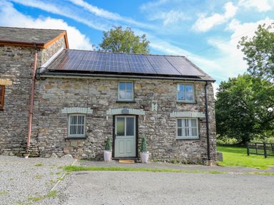 A stone cottage with solar panels on the roof and a door with two potted plants at The Old Workshop in Dre-Fach near Lampeter