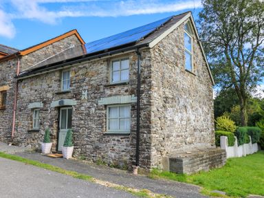 A stone house with solar panels on the roof and potted plants by the door at The Old Workshop in Dre-Fach near Lampeter