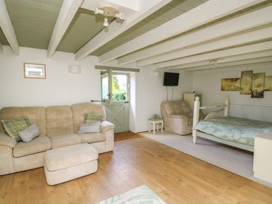 A room with a beige sofa and armchair a bed a small table with towels a wall-mounted TV and a door at The Old Workshop in Dre-Fach near Lampeter