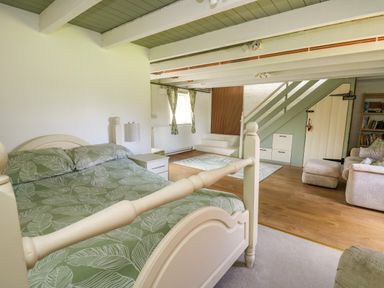 A bedroom with a bed green leaf patterned bedding and nightstand next to a sitting area with beige sofas and stairs at The Old Workshop Dre-Fach near Lampeter