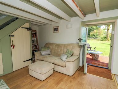 A living room with a beige sofa ottoman bookshelf under stairs and a door open to a garden at The Old Workshop Dre-Fach near Lampeter
