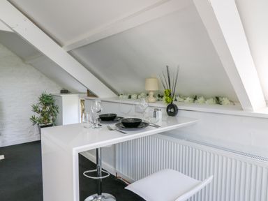 A white dining table set for two under a slanted ceiling with a white chair and a potted plant at The Old Workshop in Dre-Fach near Lampeter