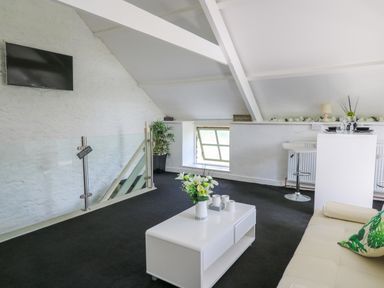 An attic living area with a white coffee table with flowers a sofa a wall-mounted television and a dining area at The Old Workshop in Dre-Fach near Lampeter